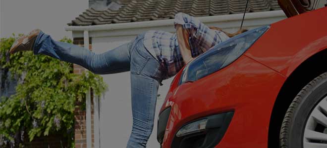 Photo of a person under the open hood of a red car checking the engine.