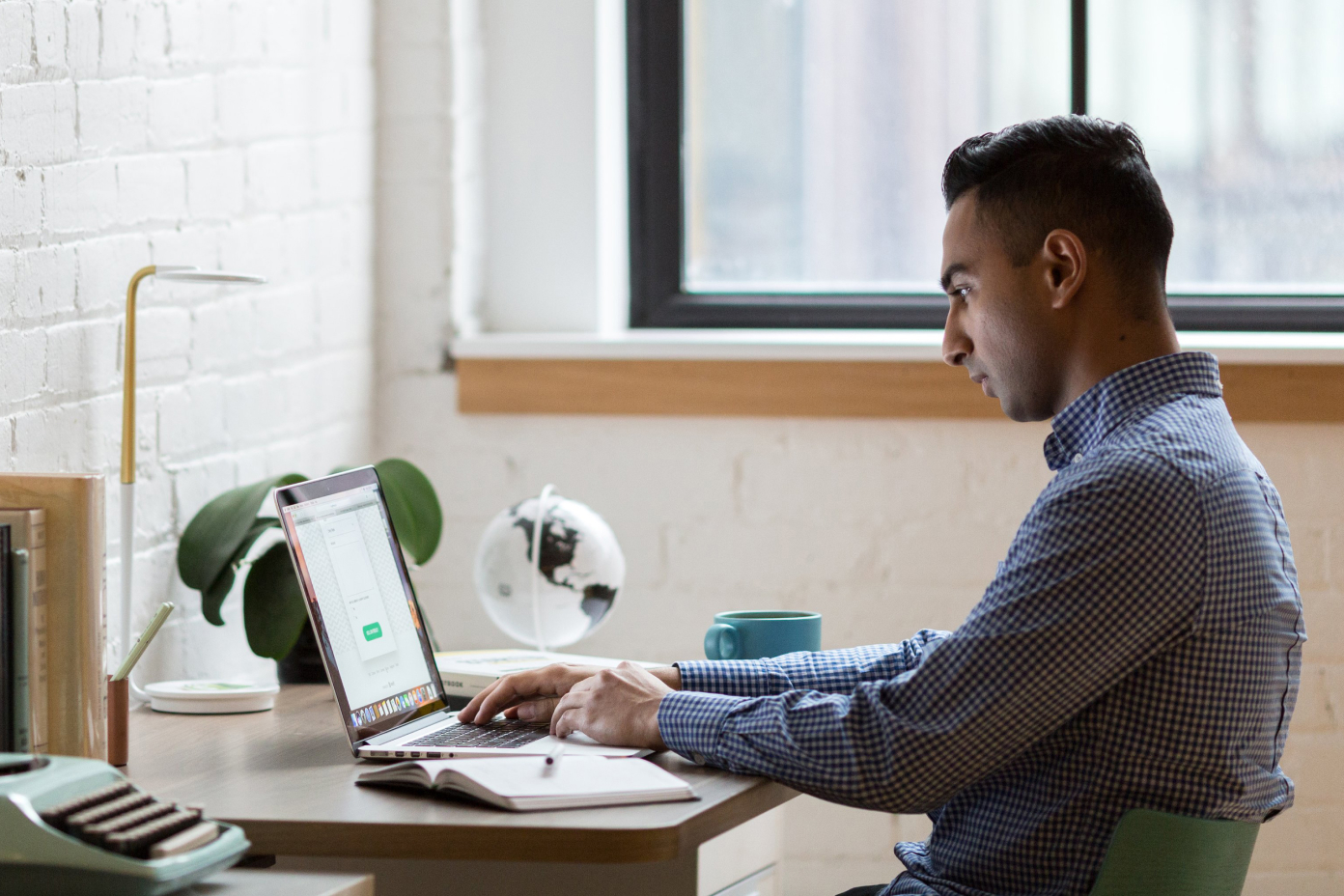 Photo of a man working on a laptop at a wooden desk in a home office.